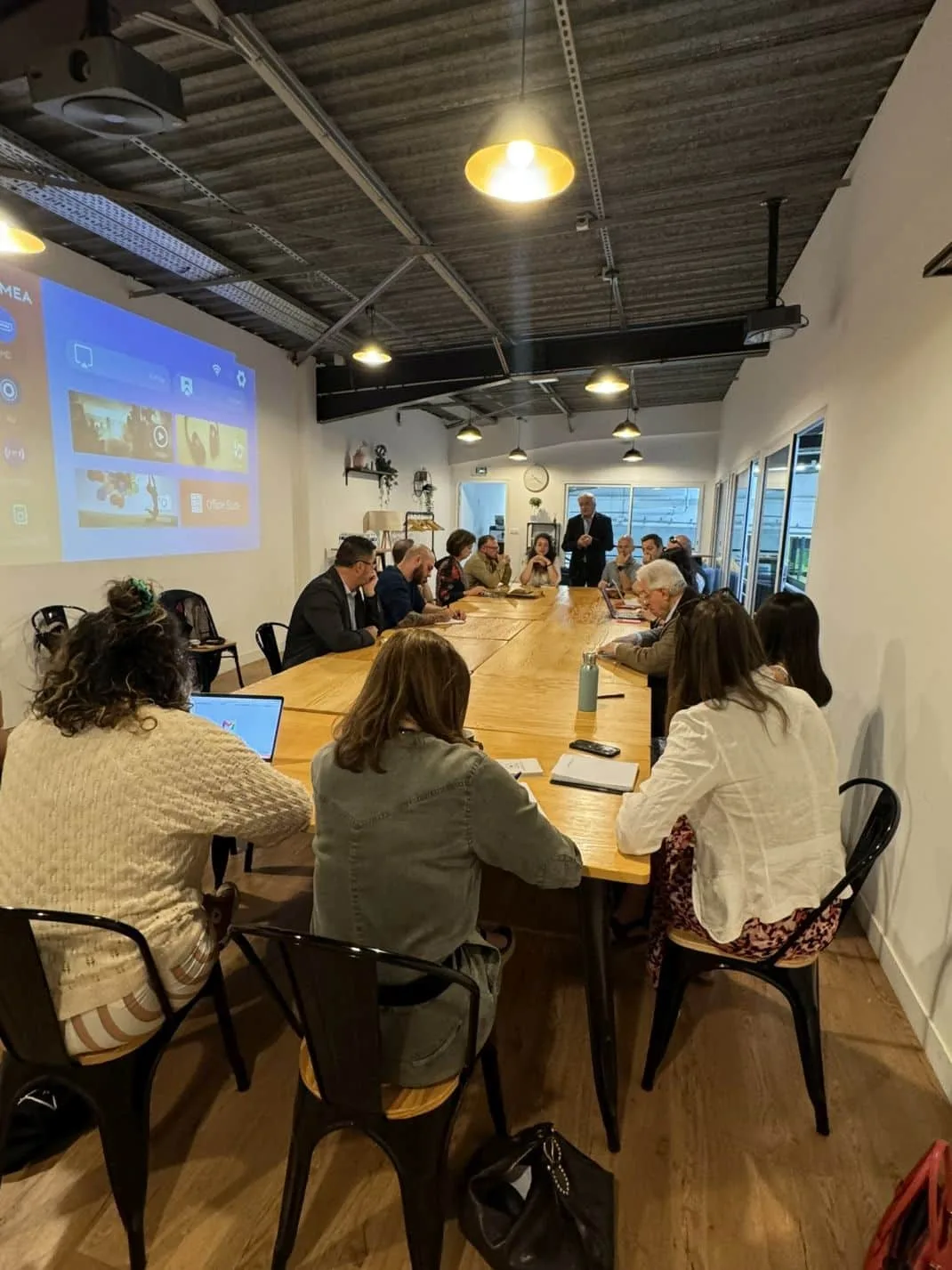 Réunion d’équipe autour de la grande table en bois du Connect Lounge, écran projeté