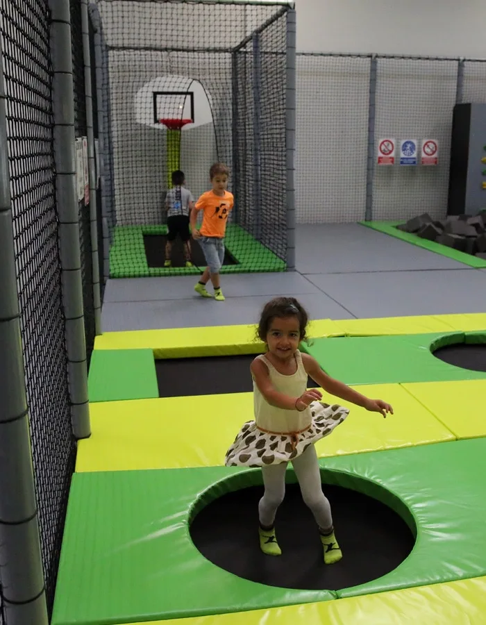 Fillette sautant sur un trampoline du mini park, deux garçons au fond
