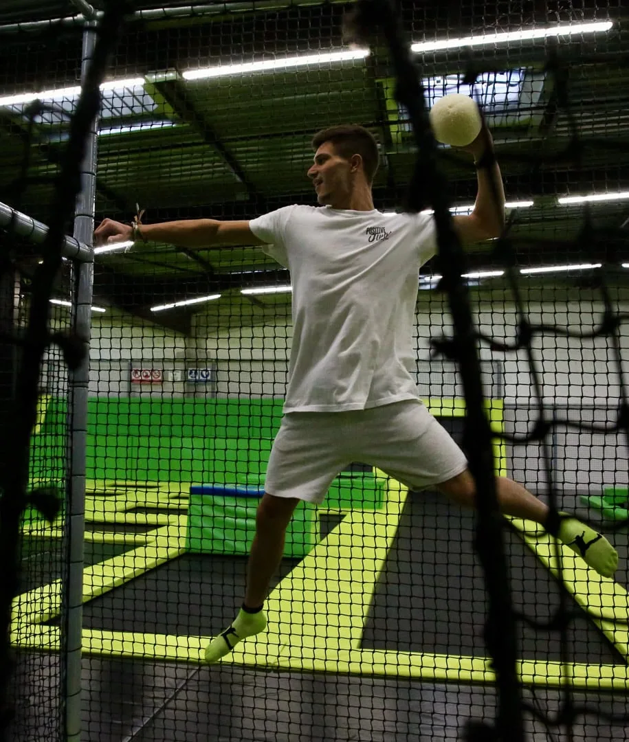 Joueur en plein saut, balle à la main, dans la cage grillagée