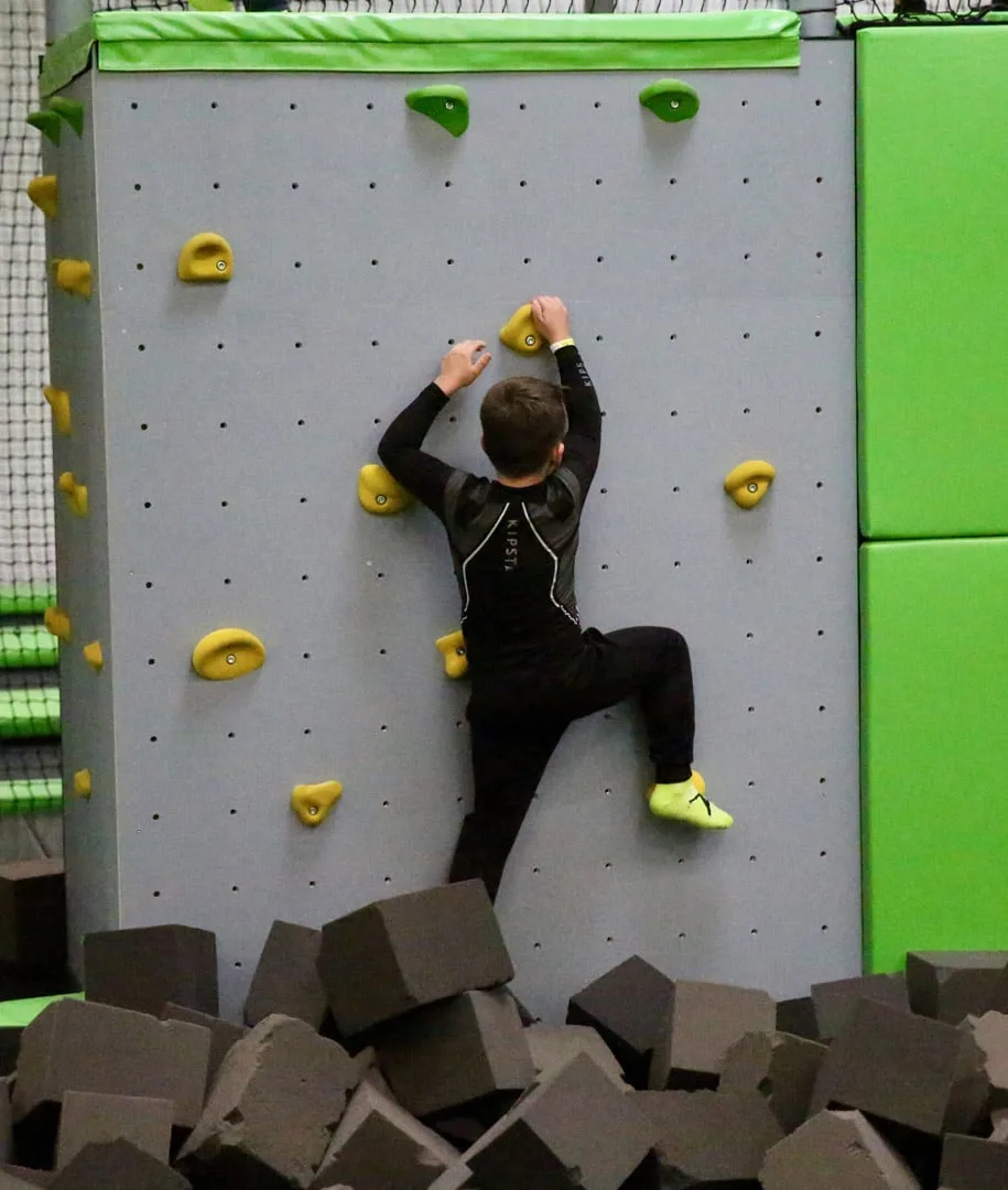 Grimpeur sur le mur à prises, au-dessus de la fosse à mousse