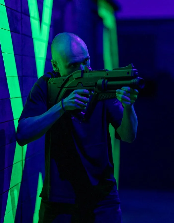 Joueur en joue dans l’arène du Laser Game, sous les néons verts et violets