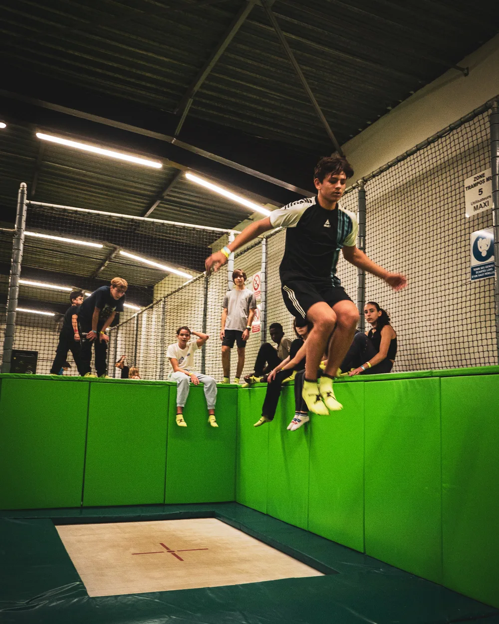 Adolescent en plein saut sur le Main Court, ses amis assis sur les murs verts