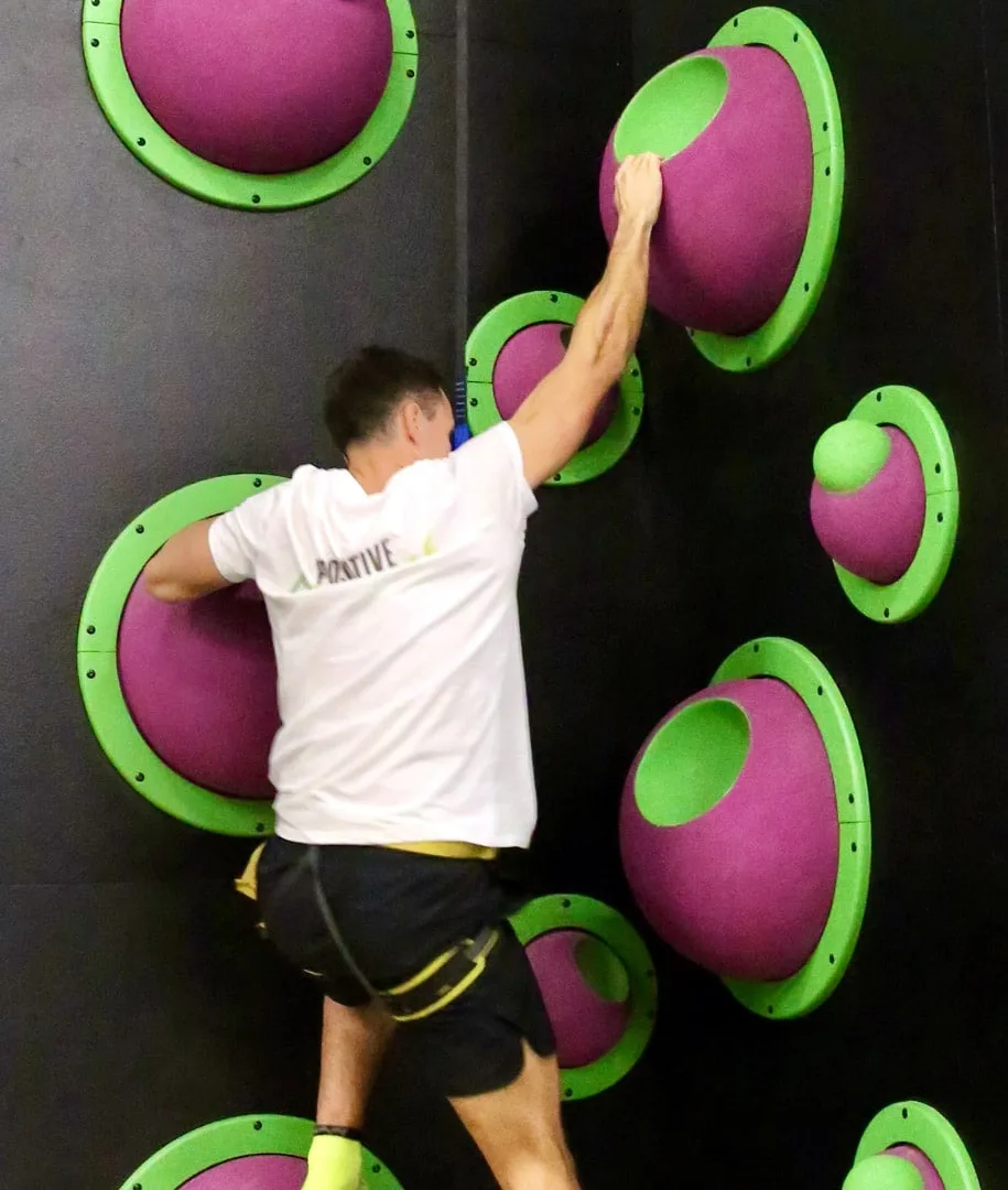 Grimpeur progressant sur les prises colorées du mur du Fun Wall