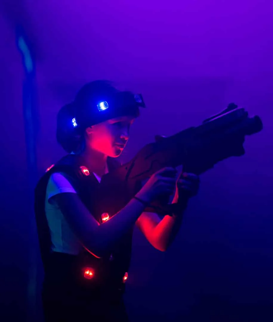 Joueuse en tenue, blaster en main, dans la lumière noire du labyrinthe