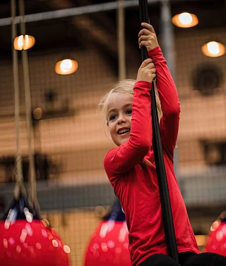 Petite fille souriante agrippée à un mât, devant les ballons rouges