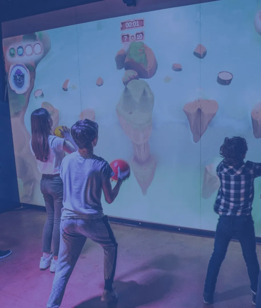 Trois enfants lancent des balles sur le mur projeté de l’arène