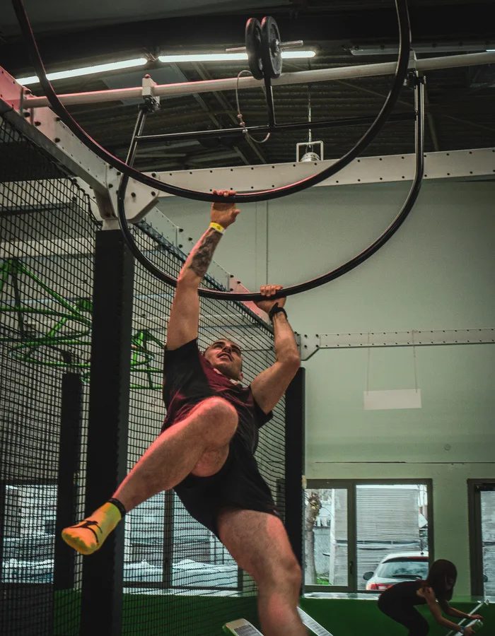 Grimpeur suspendu à l’anneau du parcours Ninja Warrior, jambes tendues