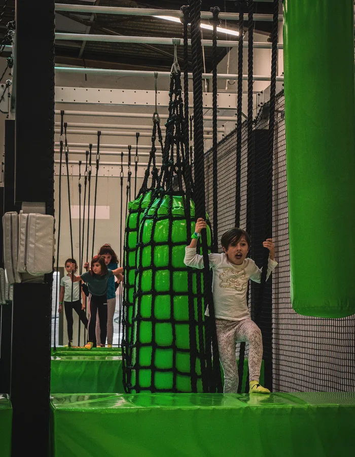 Enfant franchissant le rouleau vert du Big Bounce, le filet cargo derrière lui