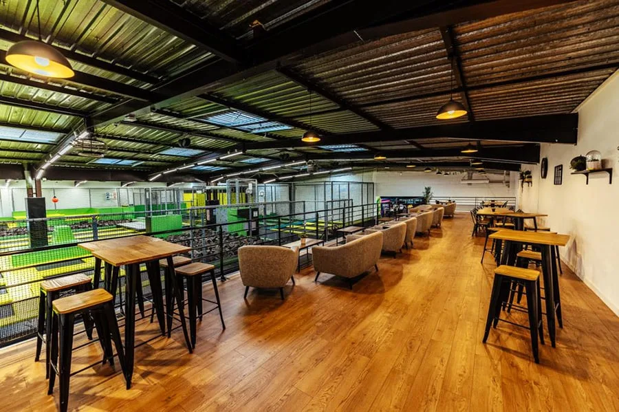 Mezzanine Jump : tables hautes et fauteuils surplombant la zone de trampolines