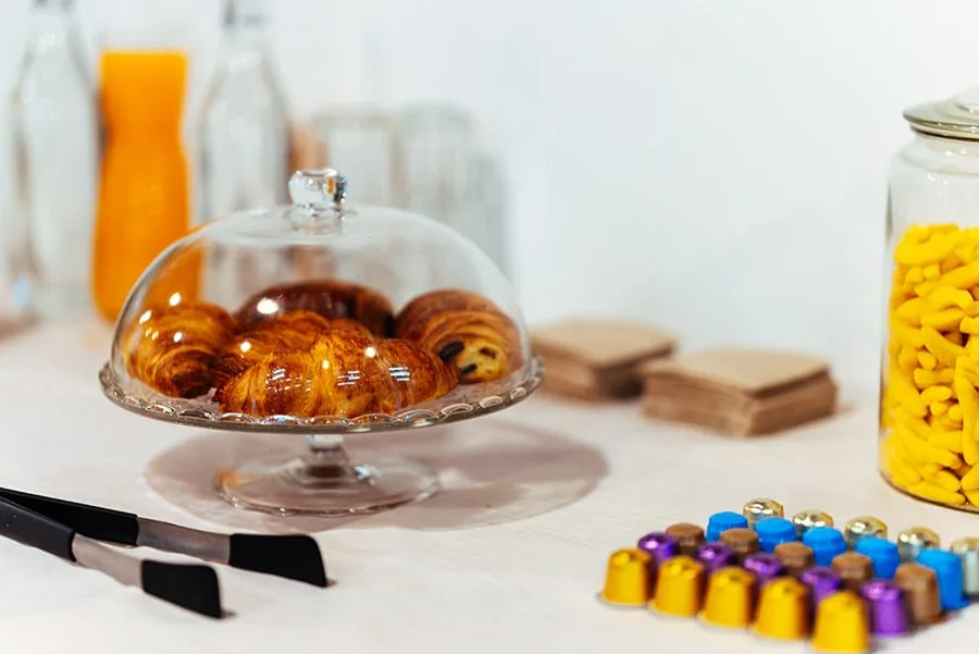 Viennoiseries sous cloche et café en capsules dressés pour une pause